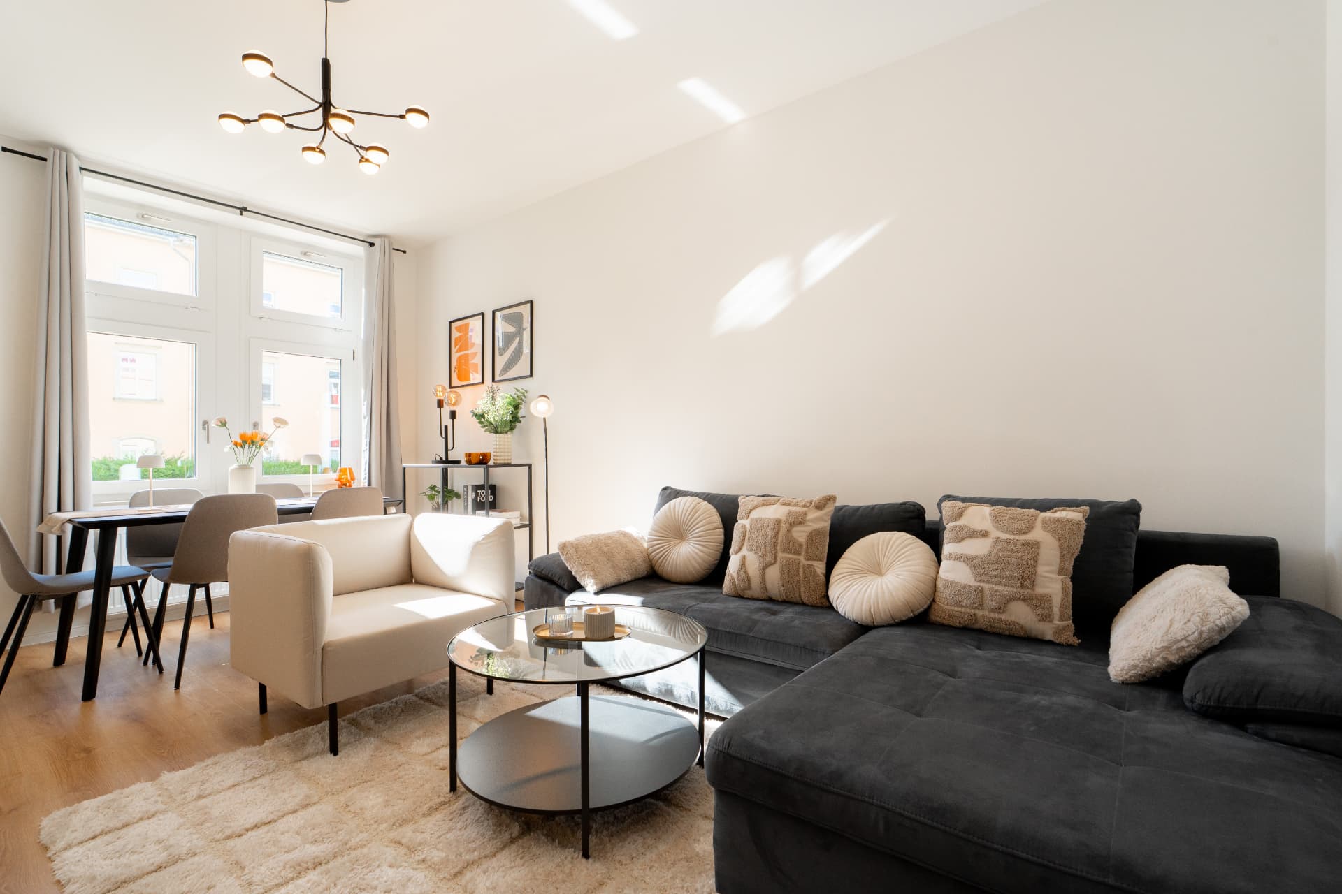 Modernes Wohnzimmer mit dunklem Ecksofa, Sessel und Esstisch am Fenster